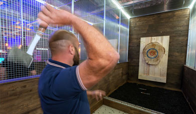 Man in blue polo shirt throwing a small axe towards a target